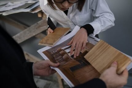 Two professionals collaborate on interior design by examining wood samples and design prints.
